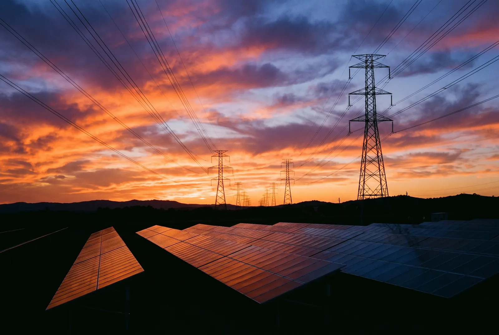 Solar panels and transmission infrastructure at sunset, illustrating grid interaction